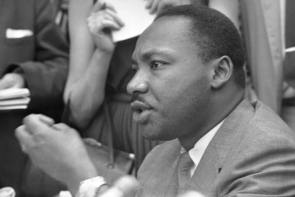صورة لمدافع حقوق الإنسان مارتن لوثر كينغ الابن أثناء حديثه، محاطًا بعدد من الأشخاص الذين يستمعون له.