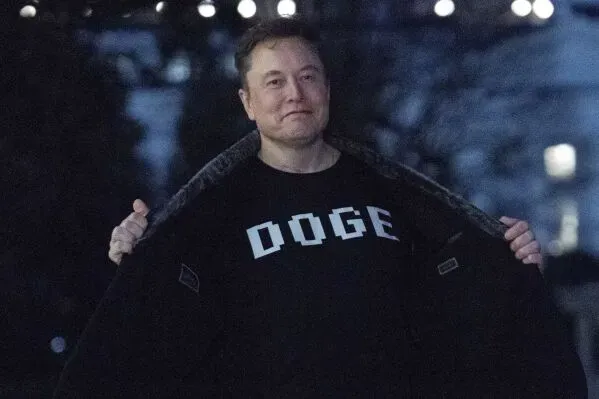 إيلون ماسك يرتدي قميصًا مكتوبًا عليه "DOGE"، مبتسمًا بينما يقف في مكان مضاء في الليل، مما يعكس تأثيره على السياسة والاقتصاد.