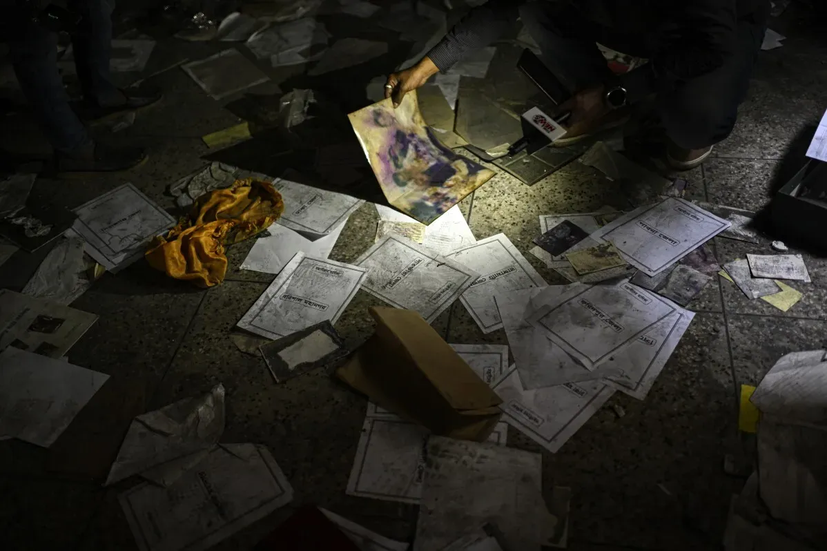 شخص يفتش بين الأوراق المبعثرة في مكان مظلم، مع وجود ضوء يسلط على مستندات وأشياء أخرى، مما يعكس الفوضى بعد الهجوم على منزل تاريخي.