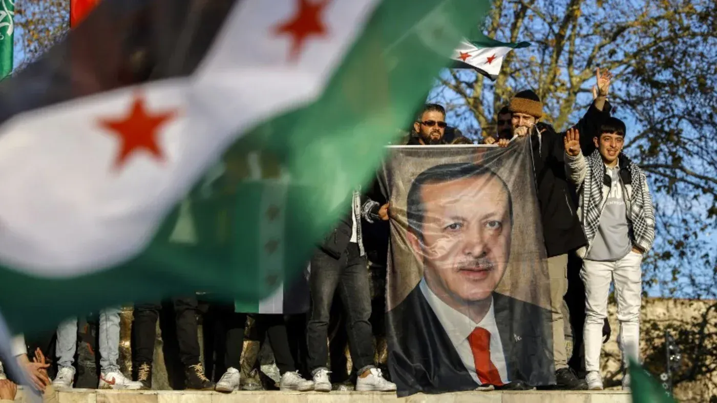 متظاهرون يحملون صورة الرئيس التركي رجب طيب أردوغان، مع أعلام سورية، في سياق الاحتجاجات حول الوضع في سوريا وتأثير تركيا.