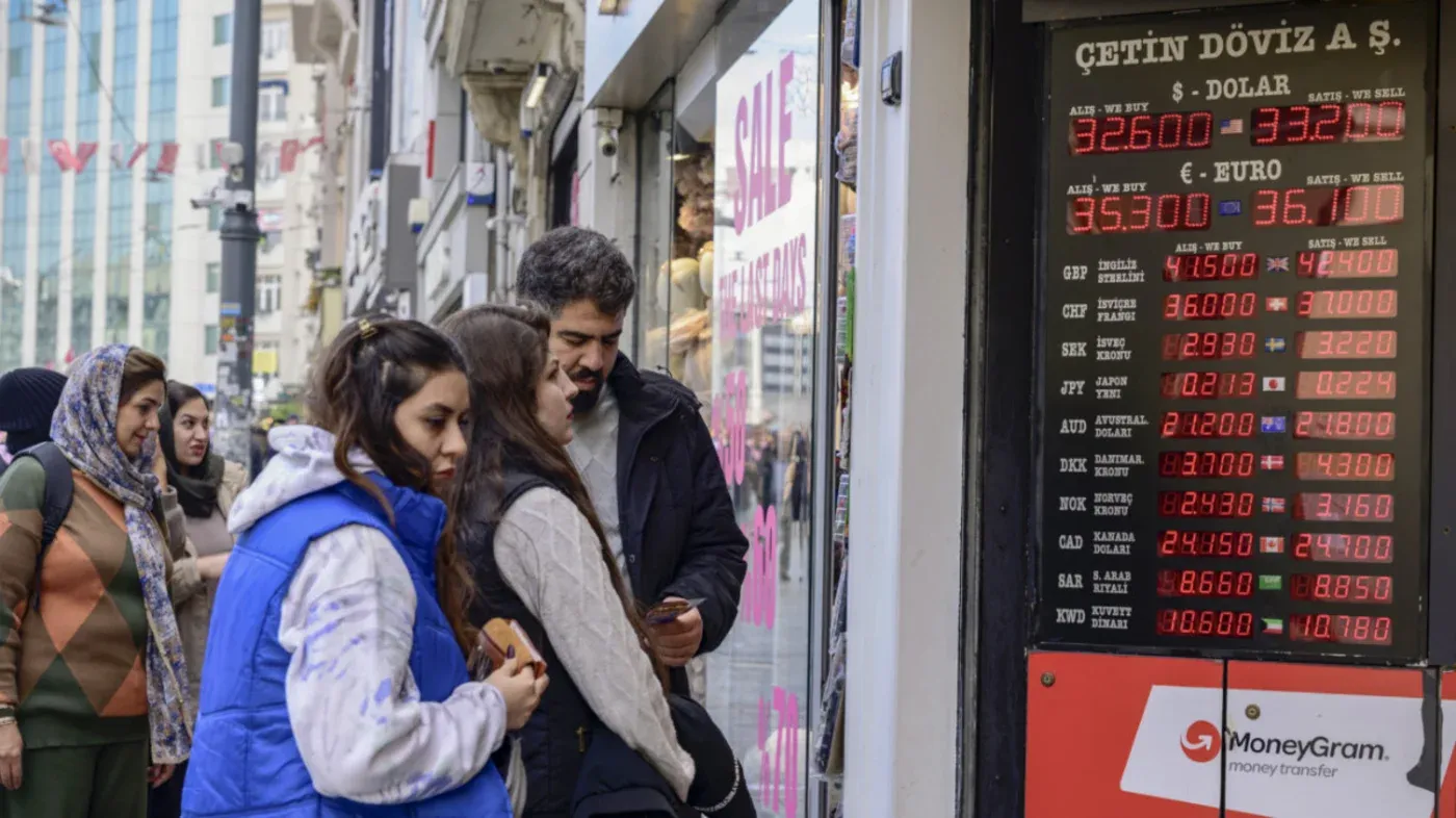 سكان يتفقدون أسعار صرف العملات الأجنبية في واجهة متجر بتركيا، حيث تظهر الأسعار المرتفعة للدولار واليورو وسط أزمة اقتصادية متزايدة.