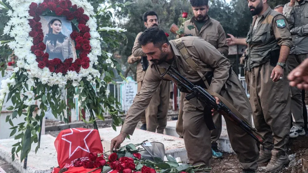 مقاتلون أكراد يضعون وروداً على قبر مغطى بعلم حزب العمال الكردستاني PKK في مراسم تأبين تعكس التوترات الإقليمية بين تركيا وإيران.
