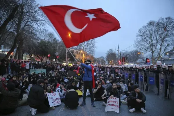 متظاهر يحمل علم تركيا وسط حشد من المحتجين الجالسين، مطالبين بالإفراج عن رئيس بلدية إسطنبول أكرم إمام أوغلو.