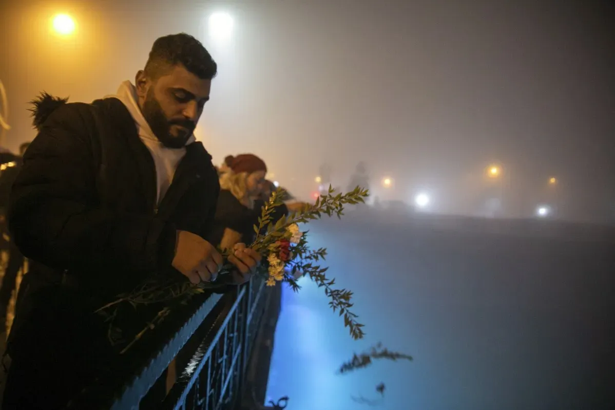 رجل يضع زهورًا على سياج في ذكرى ضحايا الزلزال المدمر في تركيا، وسط أجواء ضبابية وأضواء خافتة.