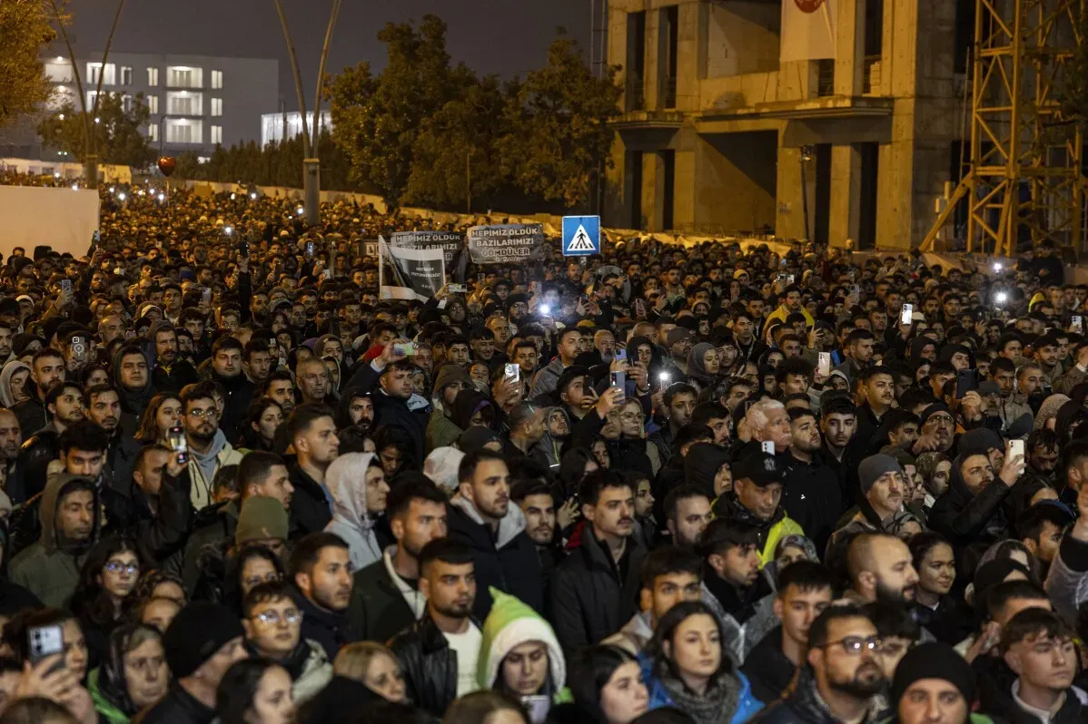 حشد كبير من الناس في إحياء ذكرى الزلزال في تركيا، يحملون الهواتف المحمولة ويظهرون علامات الحزن والتضامن.