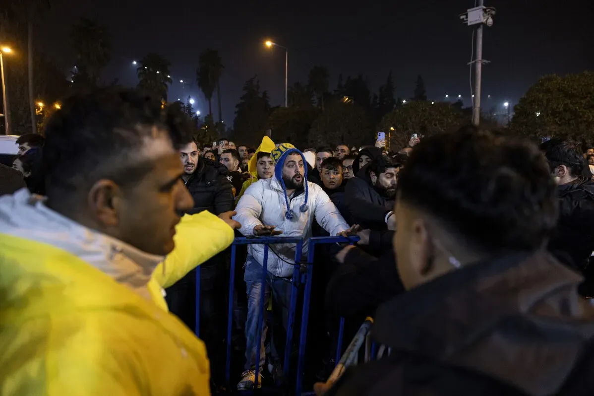 حشود من الناس تتجمع في الليل أمام حواجز أمان، مع مشاعر التوتر والقلق في أعقاب الذكرى الثانية للزلزال المدمر في تركيا.