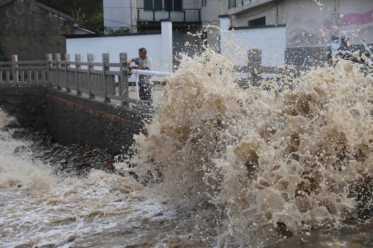 موجة عاتية من مياه البحر تضرب جدارًا ساحليًا في مقاطعة Zhejiang بالصين أثناء إعصار Bavi، مع رجل يراقب الوضع.