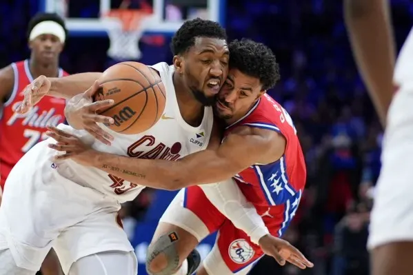 تظهر الصورة لاعب كليفلاند كافالييرز يتصارع مع لاعب من فريق 76ers على الكرة خلال مباراة حماسية، مع وجود مشجعين في الخلفية.