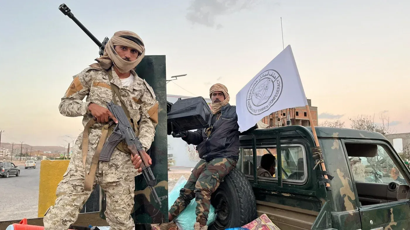 مقاتلان من المجلس الانتقالي الجنوبي في حضرموت، يحملان أسلحة، بينما ترفرف علم الجماعة في الخلفية، وسط توتر أمني متصاعد.