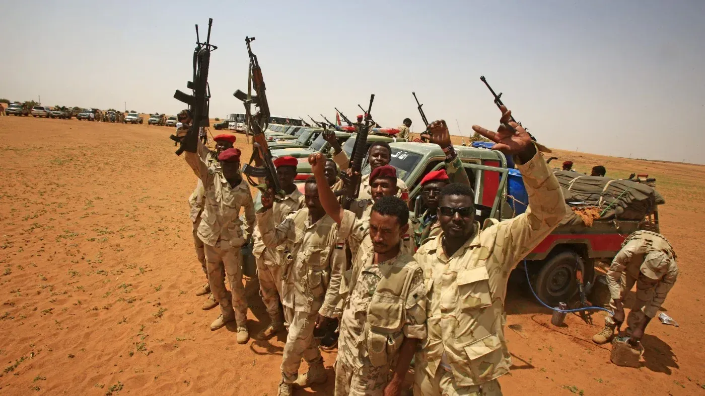 مقاتلون من قوات الدعم السريع يحملون أسلحة في منطقة صحراوية، مع ظهور عربات عسكرية خلفهم، في سياق الصراع في المثلث الحدودي.