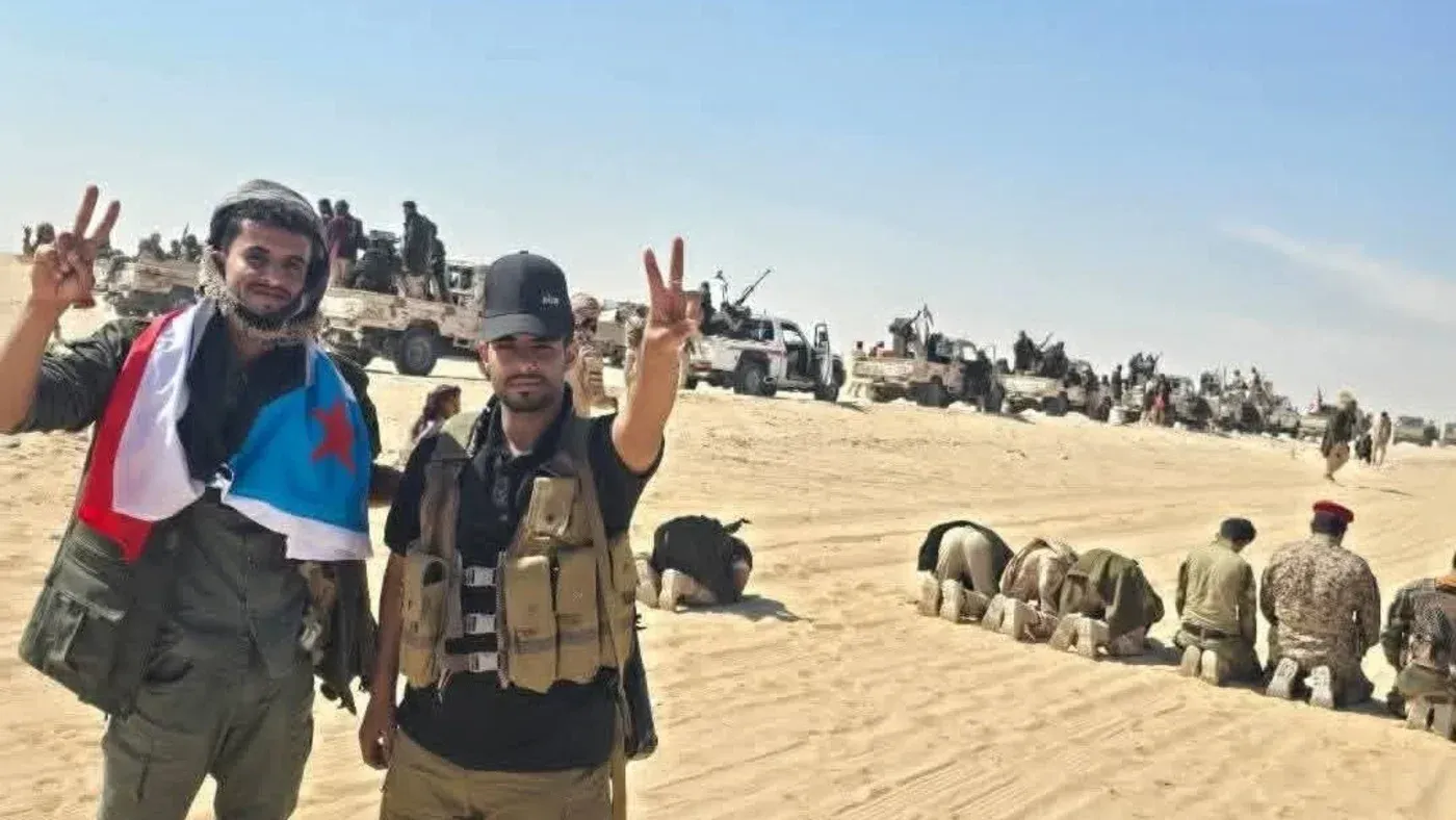 جنود من المجلس الانتقالي الجنوبي في حضرموت يرفعون علامة النصر، بينما تظهر خلفهم المركبات العسكرية في الصحراء.