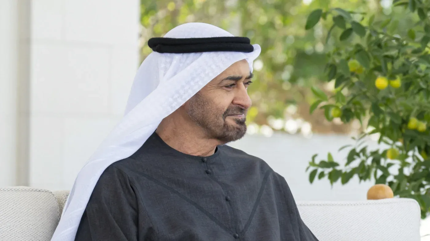 محمد بن زايد، رئيس الإمارات، يجلس في حديقة، مع خلفية خضراء، يعكس التوترات السياسية في المنطقة بعد الهجمات الإيرانية.
