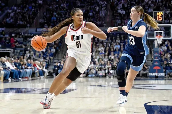 لاعبة كرة سلة من جامعة يوكون تحمل الكرة وتتجه نحو السلة، بينما تلاحقها لاعبة من فريق آخر في مباراة حماسية.