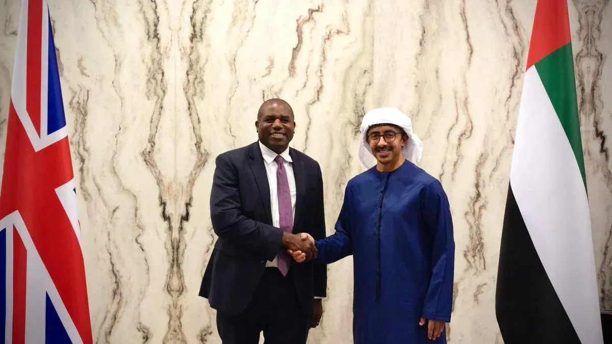 اجتماع بين مسؤول بريطاني وآخر إماراتي، مع العلم البريطاني والإماراتي في الخلفية، يعكس العلاقات السياسية بين البلدين.