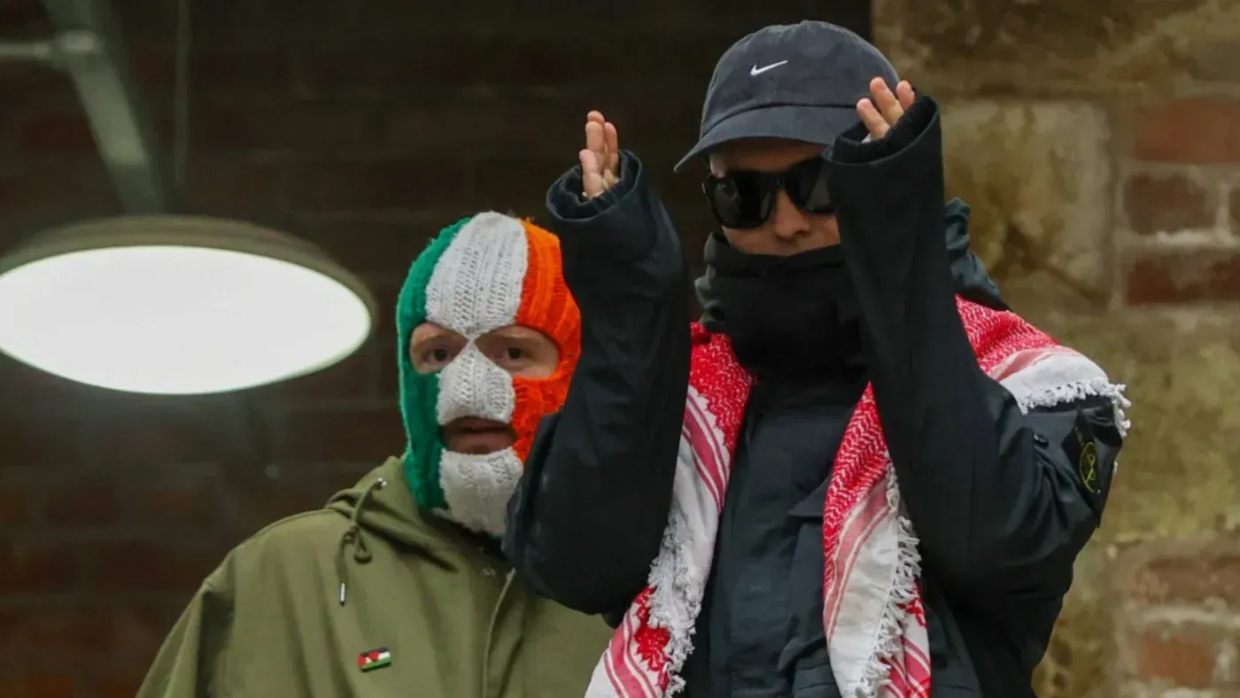 شخصان يرتديان ملابس دافئة، أحدهما يرتدي قناعًا ملونًا بعلم أيرلندا، والآخر يرتدي نظارات شمسية وشالًا فلسطينيًا، في مؤتمر صحفي.