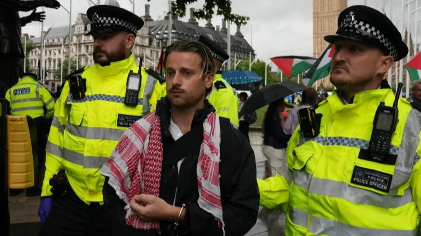 اعتقال شخص يرتدي شالًا فلسطينيًا خلال احتجاج مؤيد لفلسطين في لندن، مع وجود ضباط شرطة يرتدون زيًا أصفر.