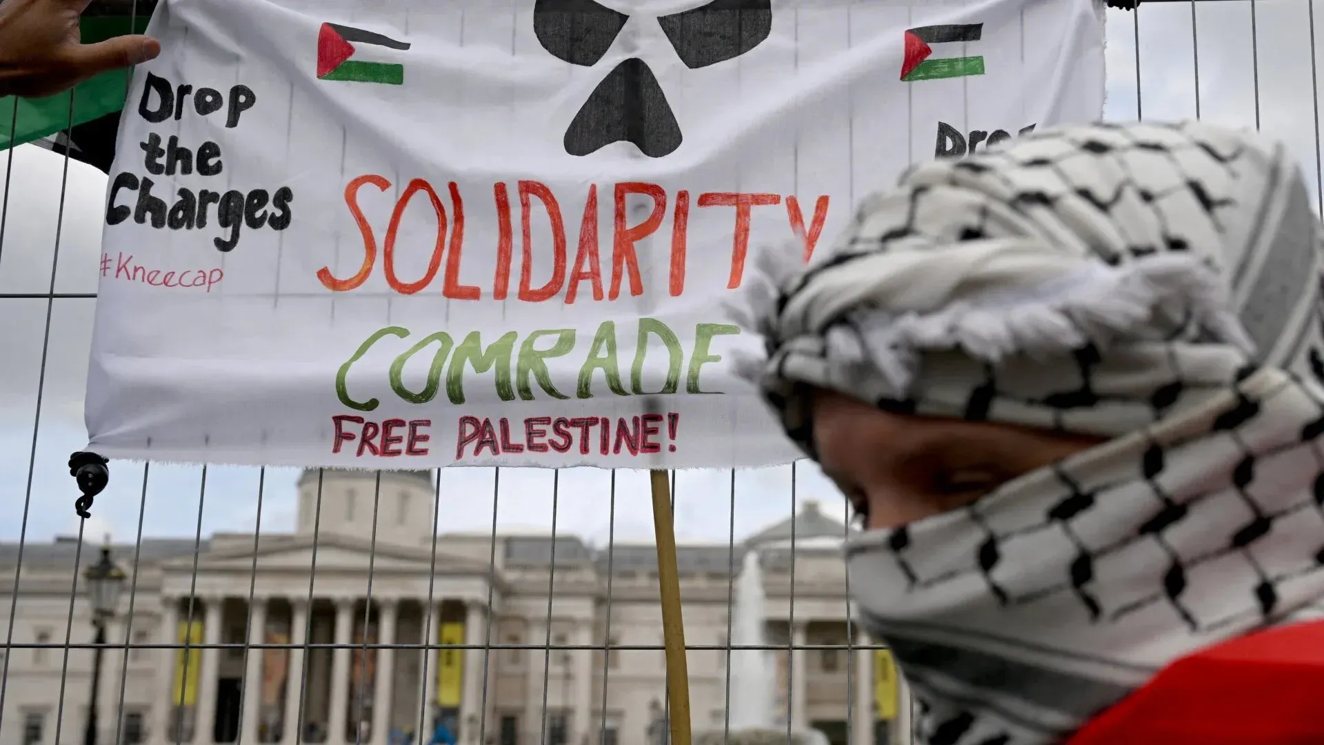 لافتة تحمل شعارات تدعو إلى دعم فلسطين، مع شخص يرتدي الكوفية، في سياق احتجاجات ضد حظر منظمة العمل الفلسطيني.