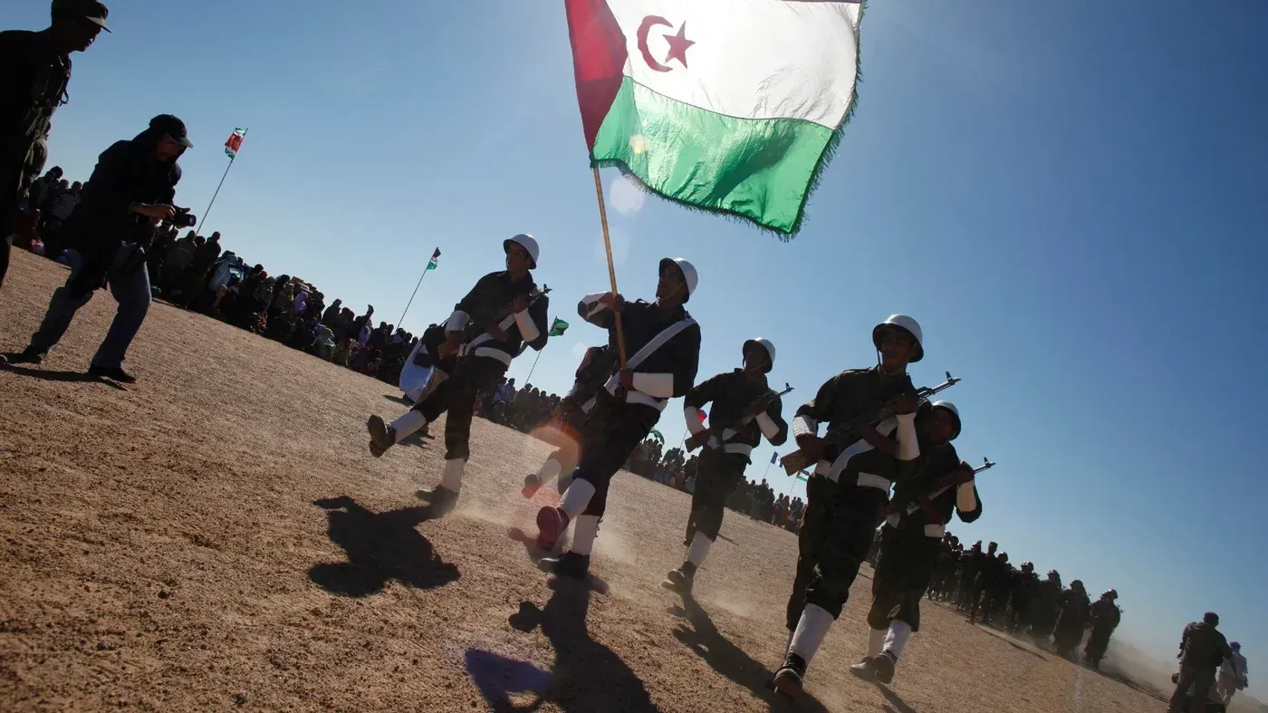 جنود من جبهة البوليساريو يحملون علم الجمهورية العربية الصحراوية خلال احتفال في الصحراء الغربية، وسط حشد من الناس.
