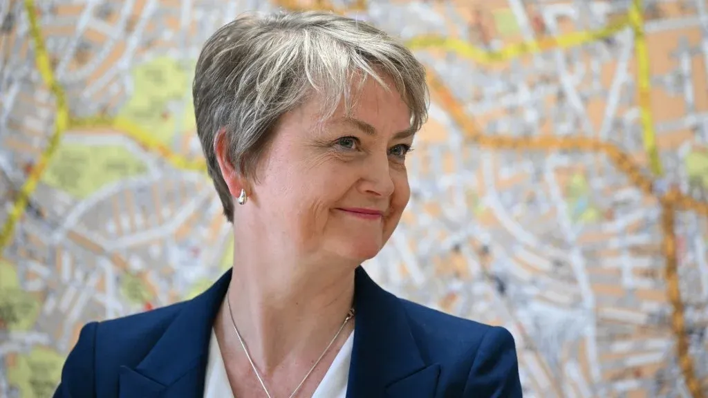 وزيرة الخارجية البريطانية Yvette Cooper مبتسمة أمام خريطة، تعلن عن عقوبات جديدة ضد الكيانات التي تمول العنف ضد الفلسطينيين.
