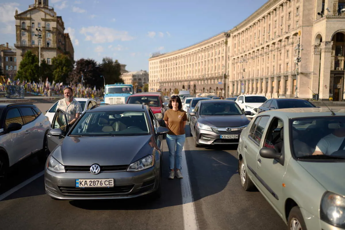 شخصان يقفان بين سيارات متوقفة في شارع رئيسي بالعاصمة الأوكرانية كييف وسط حركة مرور كثيفة تعكس تأثير الحرب على الحياة اليومية.