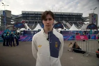 متزلج أوكراني شاب يقف أمام استاد في ميلانو، يرتدي زي التزلج، مع خلفية تعكس أجواء المنافسة الرياضية.