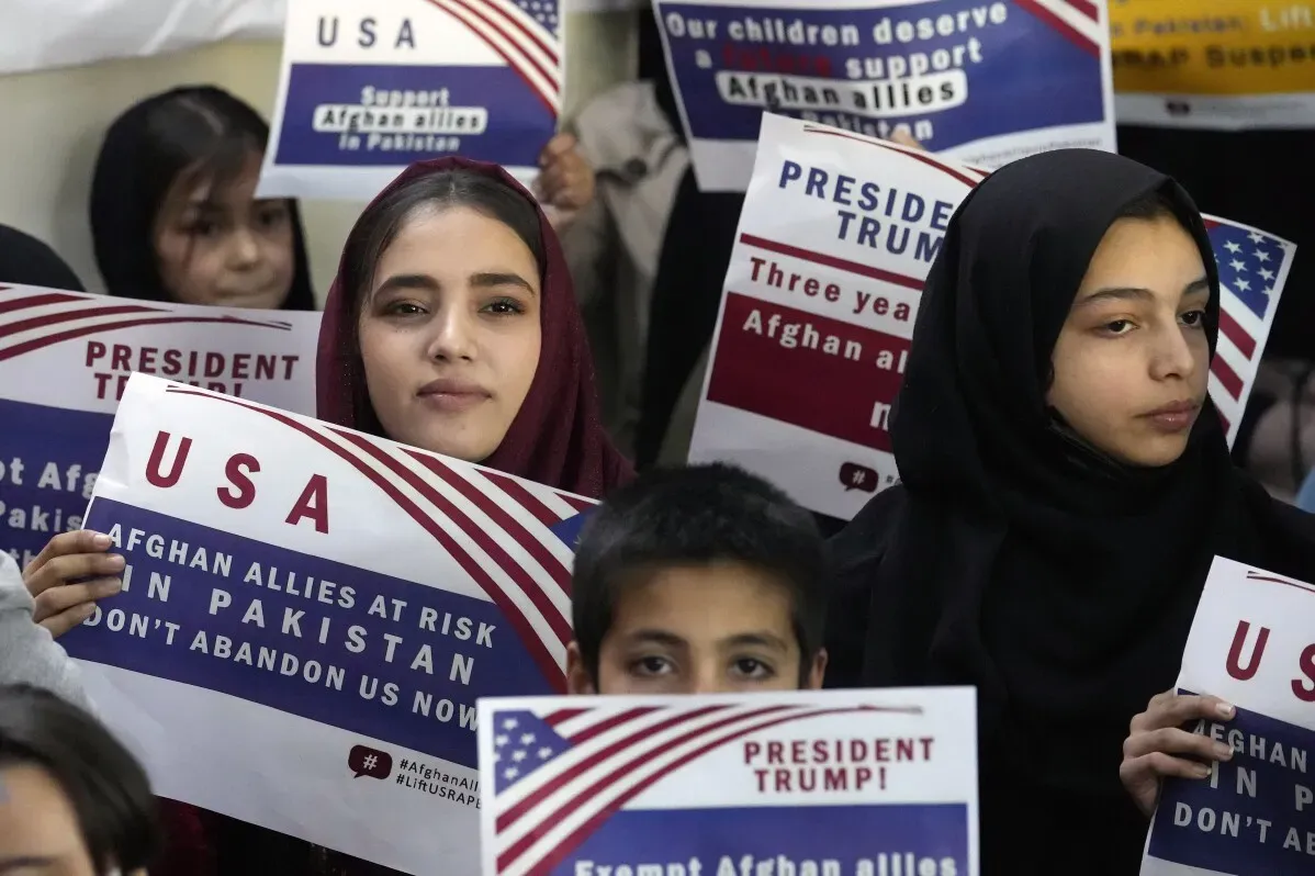 شابة ترتدي الحجاب تحمل لافتة تدعو لدعم الحلفاء الأفغان في باكستان، وسط مجموعة من الأطفال، تعبيرًا عن القلق من الترحيل.
