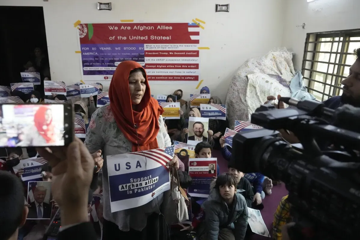 امرأة أفغانية ترتدي حجابًا تتحدث أمام مجموعة من الأطفال والبالغين الذين يحملون لافتات تطالب بدعم اللاجئين الأفغان في باكستان.