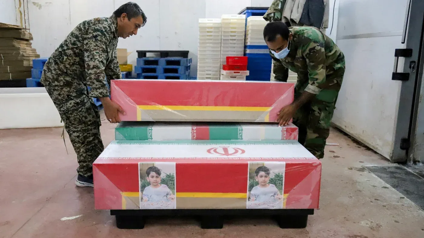 جنود إيرانيون يقومون بنقل توابيت ملونة تحمل صور أطفال ضحايا الغارة الجوية على مدرسة في مناب، في سياق التحقيقات حول الهجوم.