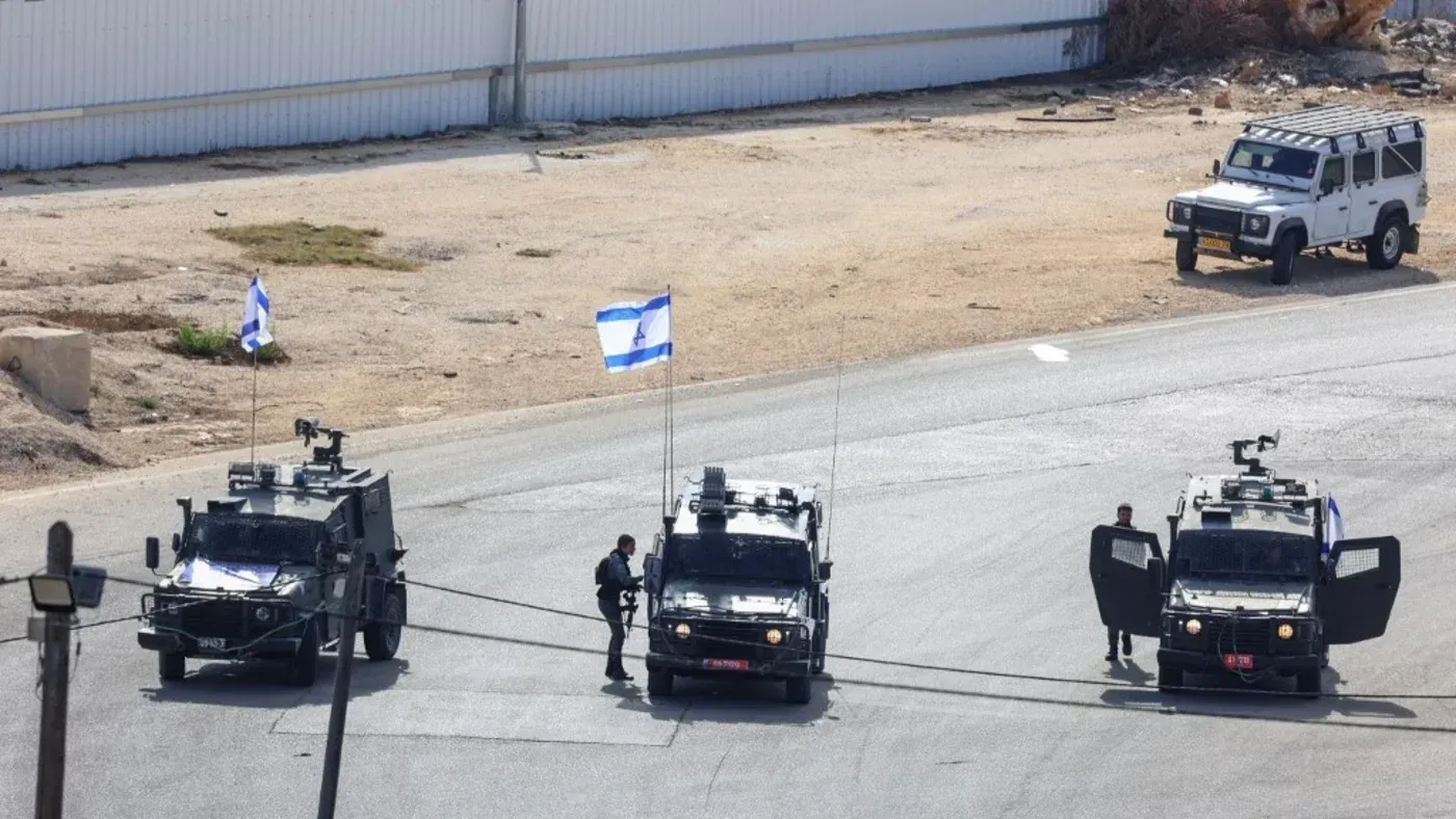 عربات مدرعة إسرائيلية تحمل الأعلام الوطنية، متوقفة في منطقة مفتوحة، تعكس التوترات الأمنية في الضفة الغربية المحتلة.