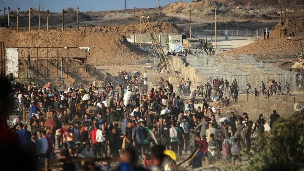 ازدحام كبير من الناس بالقرب من نقاط توزيع المساعدات في غزة، مع وجود حواجز ترابية وخدمات إنسانية في الخلفية، وسط أجواء مشحونة.