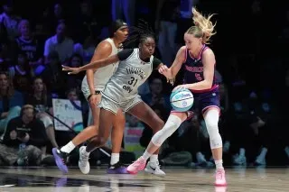 لاعبة كرة سلة تتنافس في مباراة احترافية، مع تركيز على الحركة والمهارات، بينما يشجع الجمهور في خلفية الملعب.