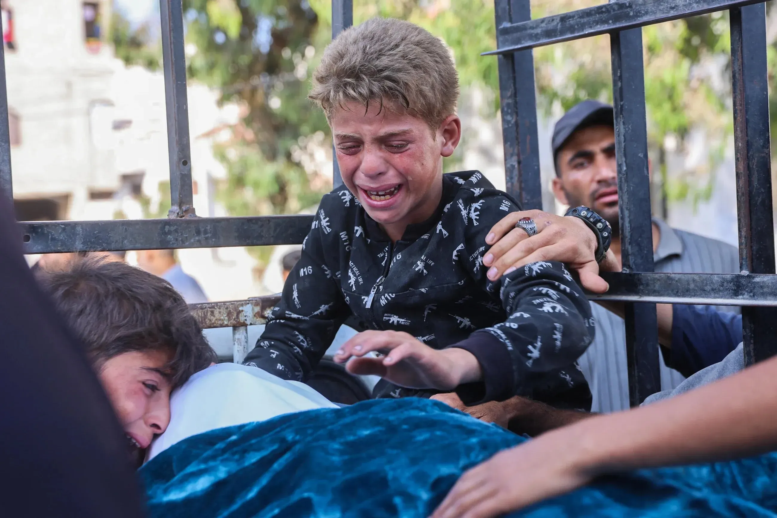 طفل يبكي بحرقة أثناء حضوره جنازة في غزة، مع مشاهد حزينة تعكس معاناة الفلسطينيين في ظل الأوضاع الإنسانية المتدهورة.