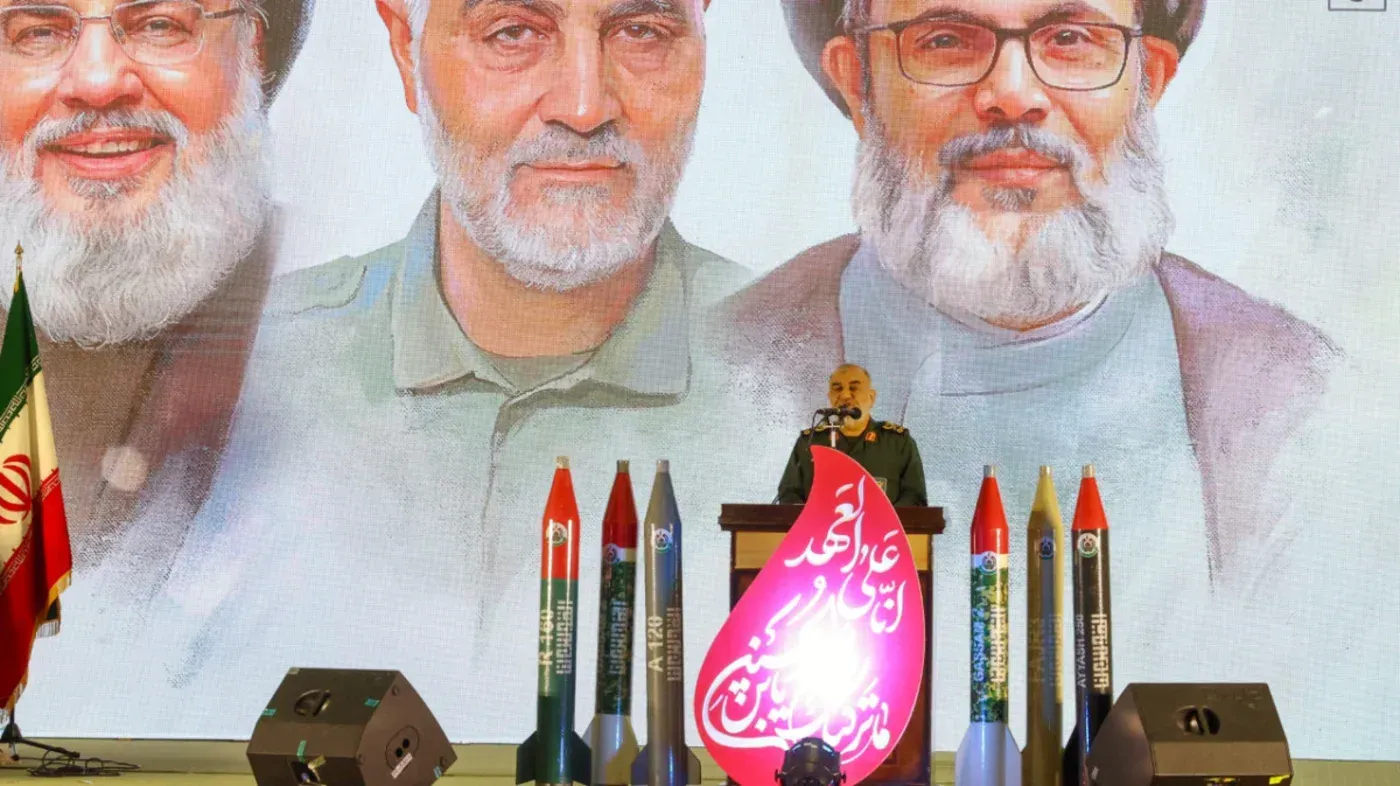 صورة لمتحدث رسمي يقف أمام منصة تحمل صواريخ، بينما تظهر في الخلفية صور لقادة إيرانيين بارزين، مما يعكس التوترات الإقليمية.