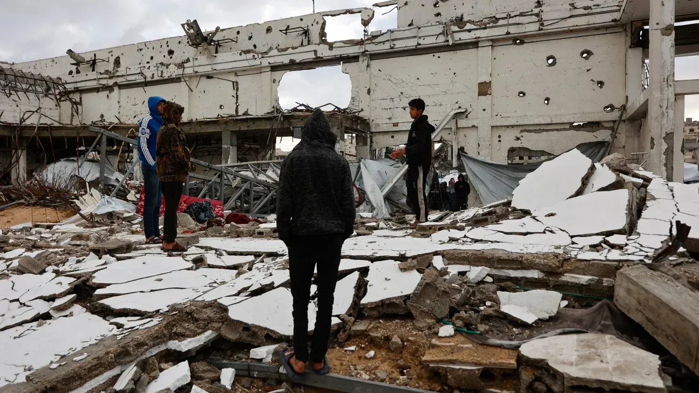 مجموعة من الأطفال يقفون وسط أنقاض مبنى مدمر في غزة، يعكس الدمار الهائل الناتج عن النزاع المستمر.