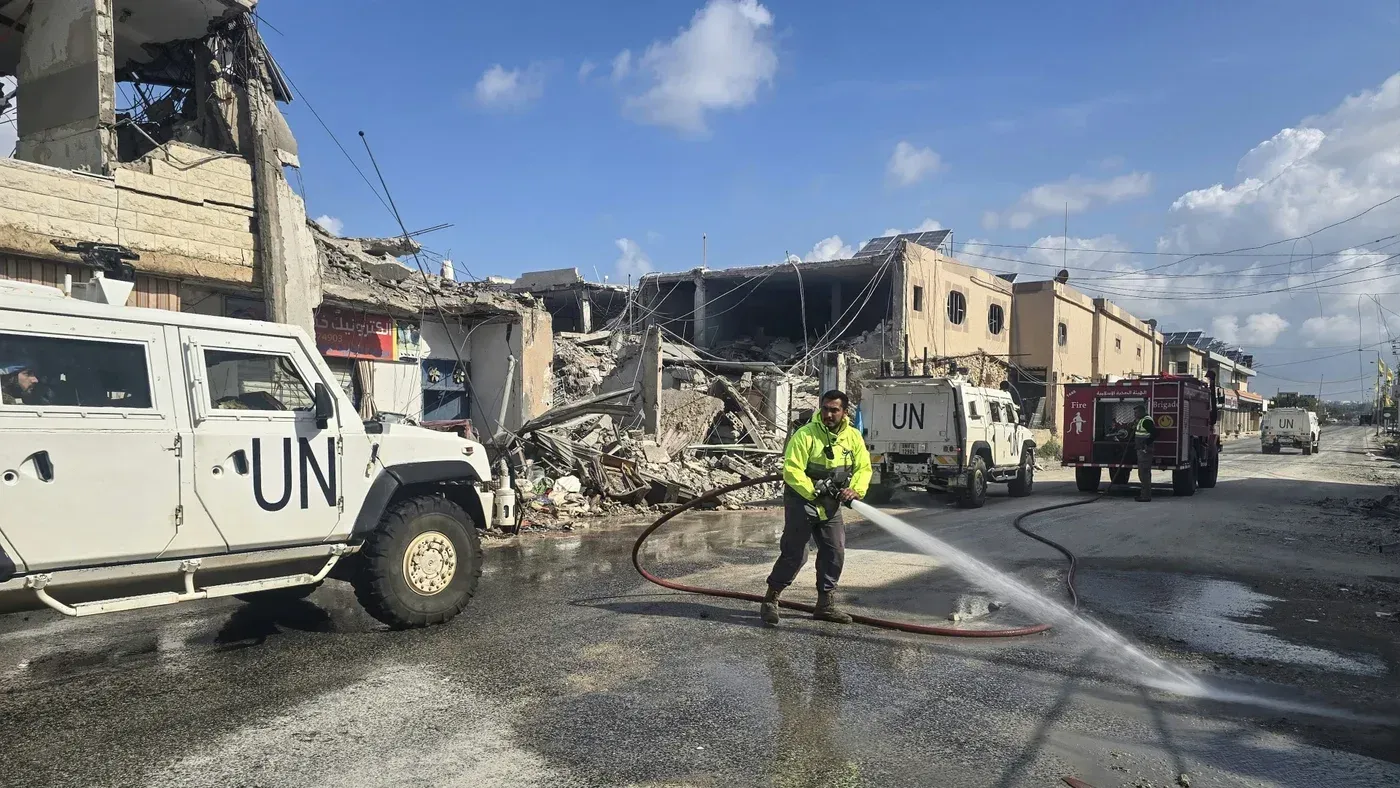 رجال إطفاء من الأمم المتحدة يعملون على إخماد حريق في منطقة مدمرة، مع وجود مركبات تابعة للأمم المتحدة في الخلفية.