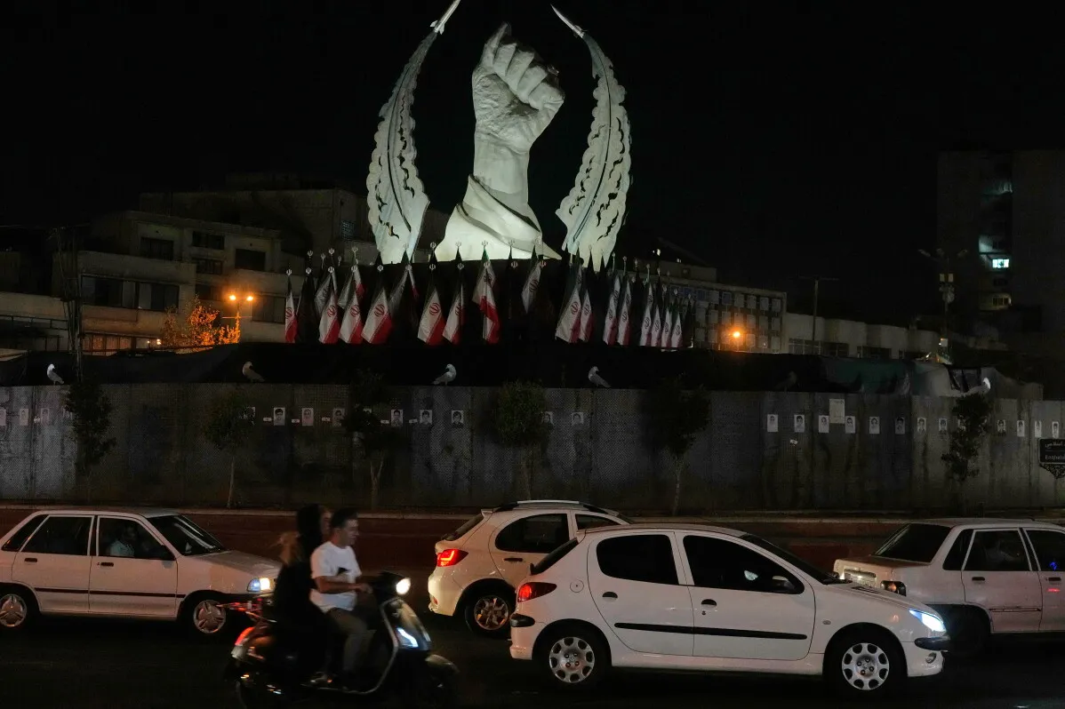 تمثال قبضة مرفوعة محاط بأعلام إيران في طهران ليلاً، يعكس تصاعد التوترات العسكرية بين الولايات المتحدة وإيران.