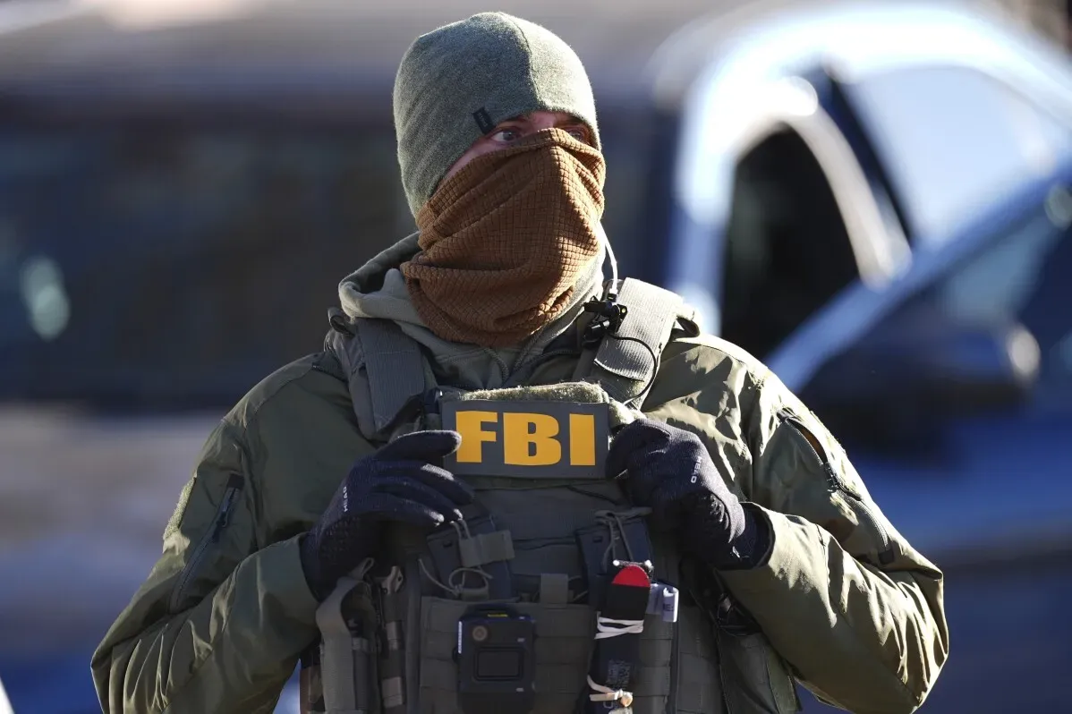 عميل من مكتب التحقيقات الفيدرالي (FBI) يرتدي زيًا عسكريًا ويظهر لافتة تحمل شعار الوكالة خلال عملية مداهمة في دنفر.