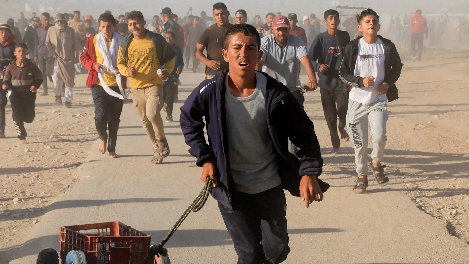 شبان فلسطينيون يركضون في حالة من الفوضى، محاولين الوصول إلى المساعدات الإنسانية في غزة، بينما تثير الأحداث المخاوف من العنف.