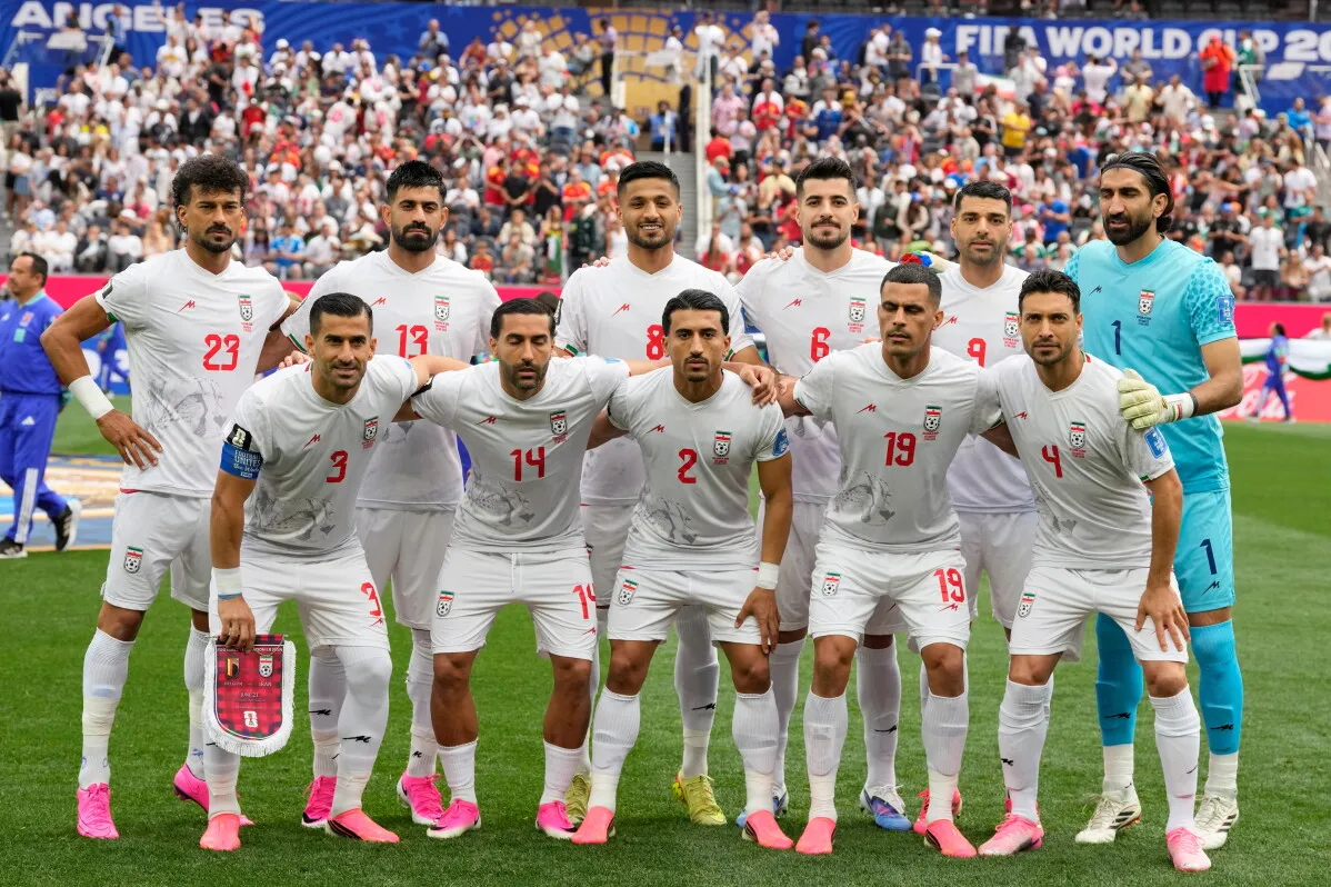 تشكيلة منتخب إيران لكرة القدم قبل مباراة كأس العالم، مع اللاعبين يرتدون الزي الأبيض في ملعب مكتظ بالجماهير.