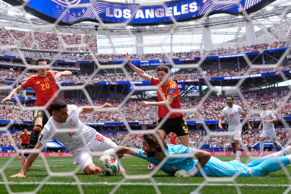 لحظة حاسمة في مباراة كأس العالم بين إيران وإسبانيا، حيث يحاول لاعب إيراني تسجيل هدف بينما يحمي الحارس مرماه، مع جمهور كبير في الخلفية.