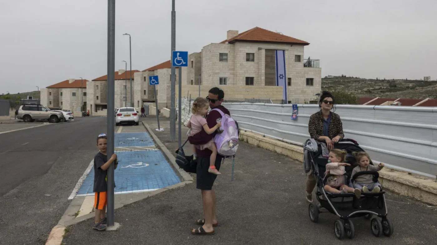 عائلة إسرائيلية تتجول في مستوطنة بالضفة الغربية، مع وجود لافتات تشير إلى خدمات قنصلية جديدة للمستوطنين.