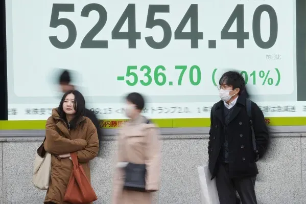 تظهر الصورة متداولين في طوكيو يقفون أمام شاشة تعرض انخفاض مؤشر نيكاي 225 بنسبة 0.7%، مما يعكس حالة عدم اليقين في الأسواق الآسيوية.