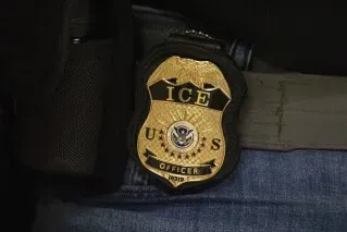 شعار وكالة إنفاذ قوانين الهجرة والجمارك الأمريكية، يظهر تفاصيل الشعار المعدني مع كلمة "ضابط" أسفلها، مما يبرز دور الوكالة في قضايا الهجرة.