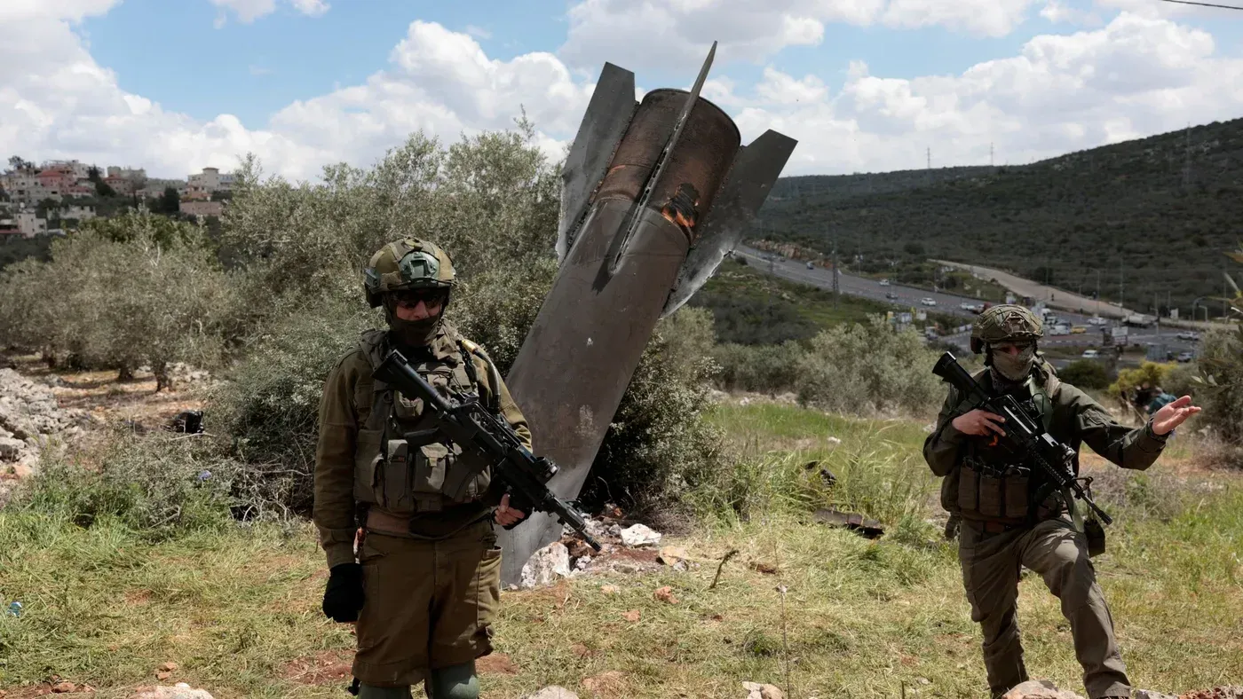 جنود إسرائيليون يقفون بجانب حطام صاروخ في منطقة جبلية، مما يعكس التوترات العسكرية مع إيران وتأثيرها على الأمن الإقليمي.