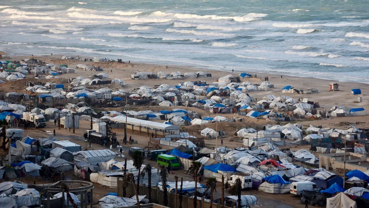 مخيمات للاجئين الفلسطينيين على شاطئ غزة، تظهر الخيام البيضاء والزرقاء وسط الأمواج، تعكس معاناة السكان في ظل النزاع المستمر.
