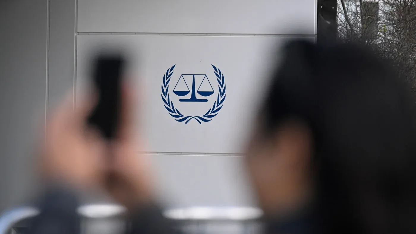شعار المحكمة الجنائية الدولية على جدار خارجي مع أشخاص يلتقطون صورًا، في سياق العقوبات الأمريكية المثيرة للجدل ضد المحكمة ومنظمات حقوق الإنسان.