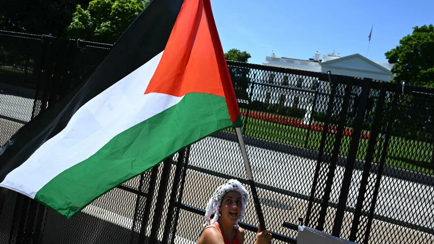 امرأة تحمل علم فلسطين أمام سياج البيت الأبيض، تعبر عن دعمها للقضية الفلسطينية وسط تزايد التوترات الدولية.