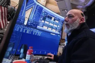 متداول في بورصة نيويورك يراقب الشاشات ويحلل البيانات المالية، مع التركيز على حركة السوق بعد تراجع ترامب عن الرسوم الجمركية.