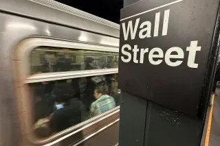 تظهر الصورة لافتة "Wall Street" في محطة مترو، مع وجود ركاب داخل القطار، مما يعكس النشاط المالي في الأسواق الأمريكية.