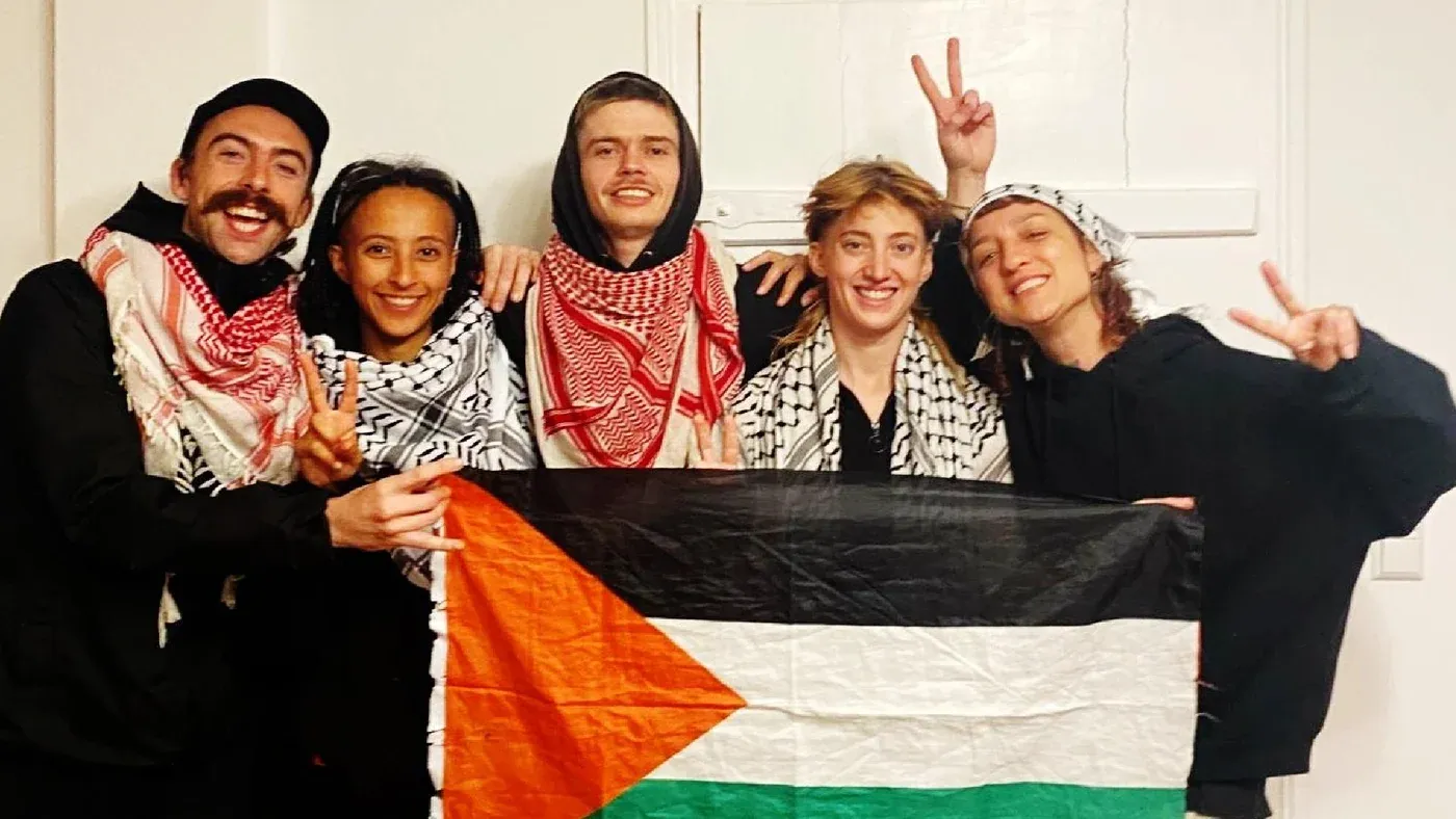 مجموعة من الناشطين يحملون علم فلسطين، يرتدون الكوفية، ويظهرون إشارات النصر، تعبيراً عن دعمهم للقضية الفلسطينية.